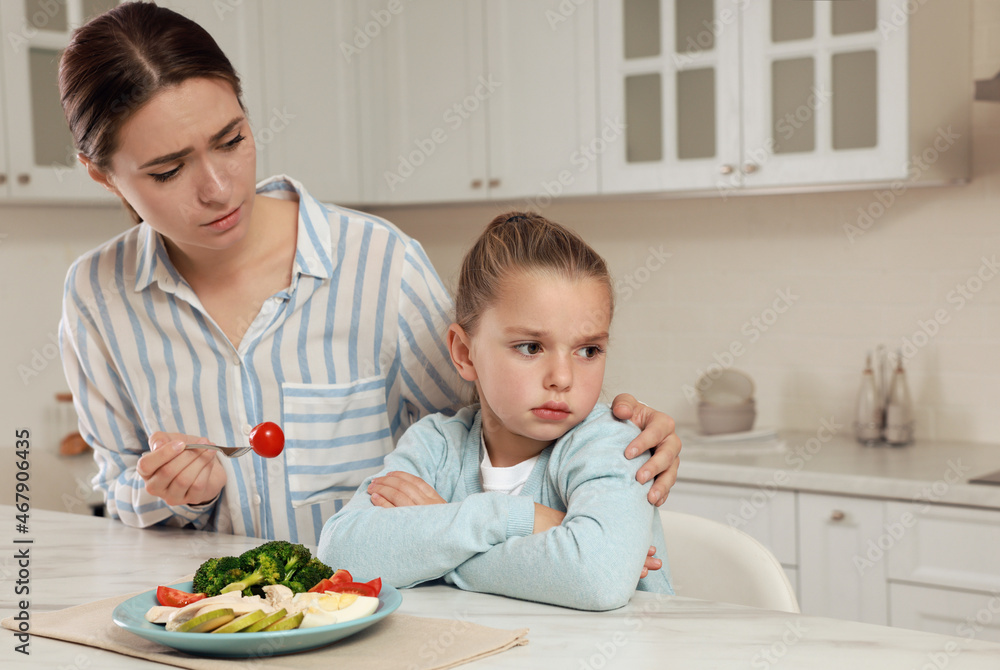 Mother feeding her daughter in kitchen. Little girl refusing to eat dinner Mother feeding her daughter in kitchen. Little girl refusing to eat dinner