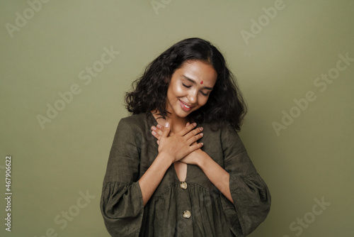 Young south asian woman with bindi smiling while holding hands on her chest photo