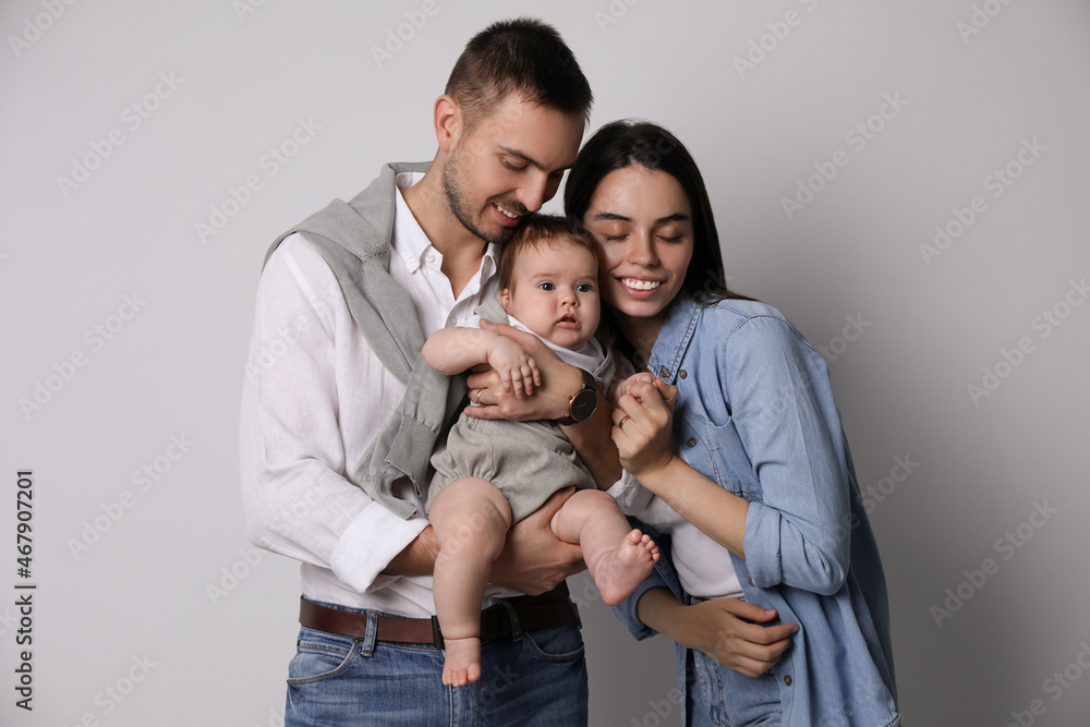 Happy family. Couple with their cute baby on grey background Happy family. Couple with their cute baby on grey background