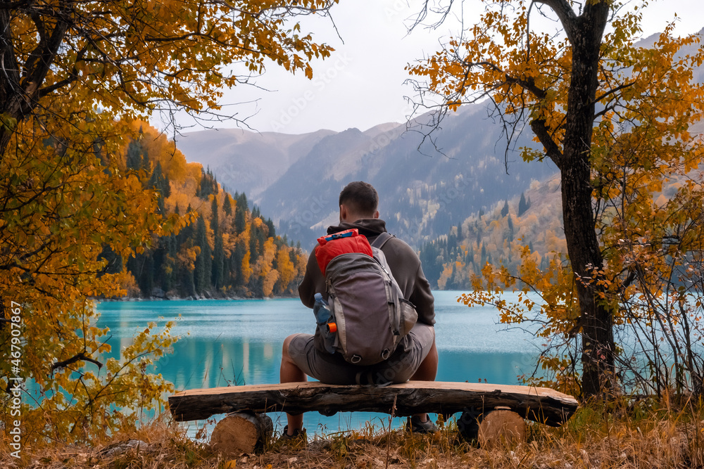 Tourist is resting on the bench near beautiful mountains lake with turquoise water and colorful forest. Tourism, trekking, hiking in autumn concept. Tourist is resting on the bench near beautiful mountains lake with turquoise water and colorful forest. Tourism, trekking, hiking in autumn concept.