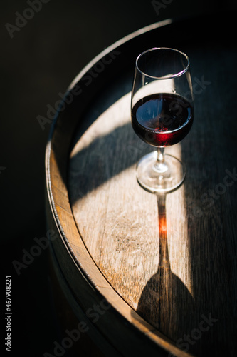 Glass of Porto wine on a wooden oak barrel with long shadow in moody atmosphere 