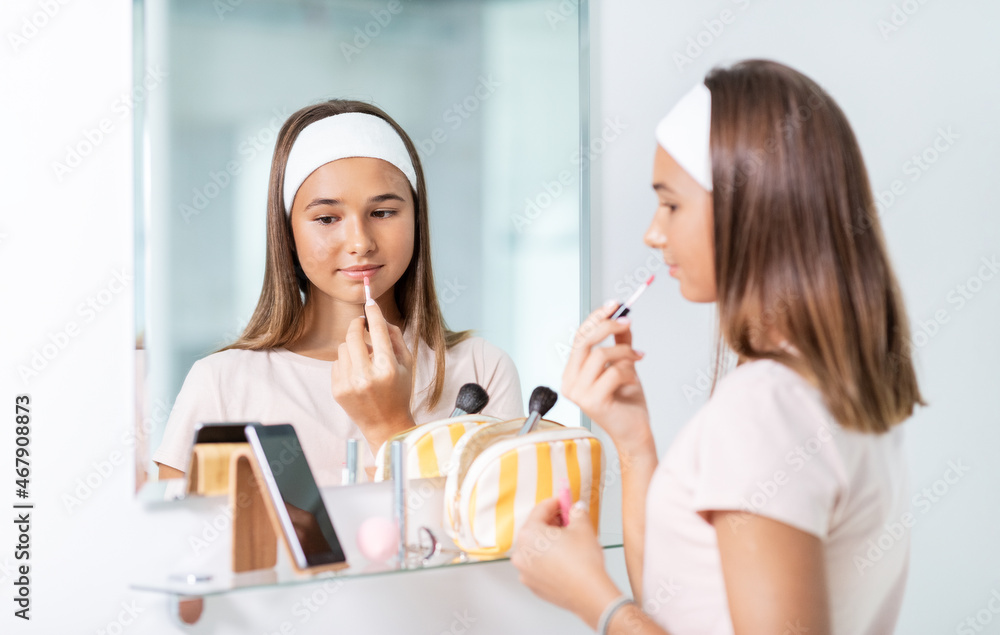 beauty, make up and cosmetics concept - teenage girl applying lip gloss and looking to mirror at home bathroom beauty, make up and cosmetics concept - teenage girl applying lip gloss and looking to mirror at home bathroom