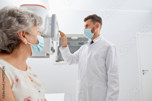 Side view professional radiologist touching screen of modern equipment starting scanning process. Old grey female patient waiting  examine health in modern clinic. Concept of medicine.