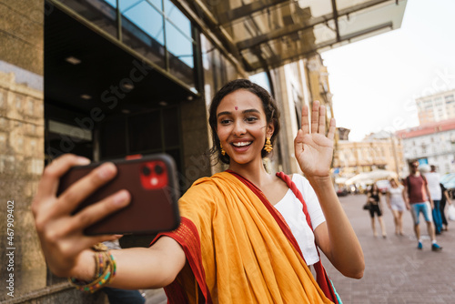 Photography Young indian woman wearing sari taking selfie on cellphone at city street