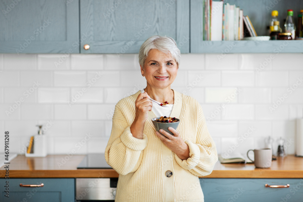 © Syda Productions - breakfast, food and people concept - happy smiling woman with spoon eating cereal on kitchen at home