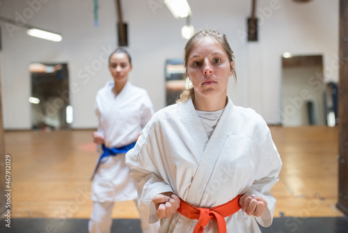 Determined young women at karate training. Attractive women in white clothes with blue and red belts warming up before training. Sport, healthy lifestyle concept