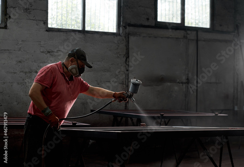 Caucasian man painting metal construction using spray gun. Industrial worker wearing protective mask and gloves at work. Concept of service and renovation.