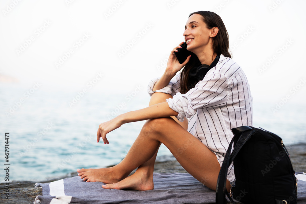 Happy young woman relaxing on the sandy beach. Beautiful woman talking to the phone..