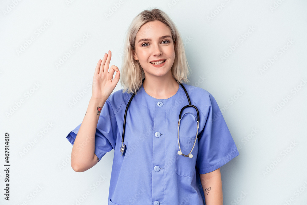 Young nurse woman isolated on blue background cheerful and confident showing ok gesture. Young nurse woman isolated on blue background cheerful and confident showing ok gesture.