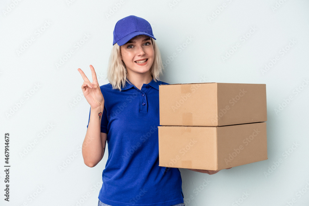 Young delivery caucasian woman isolated on blue background joyful and carefree showing a peace symbol with fingers. Young delivery caucasian woman isolated on blue background joyful and carefree showing a peace symbol with fingers.