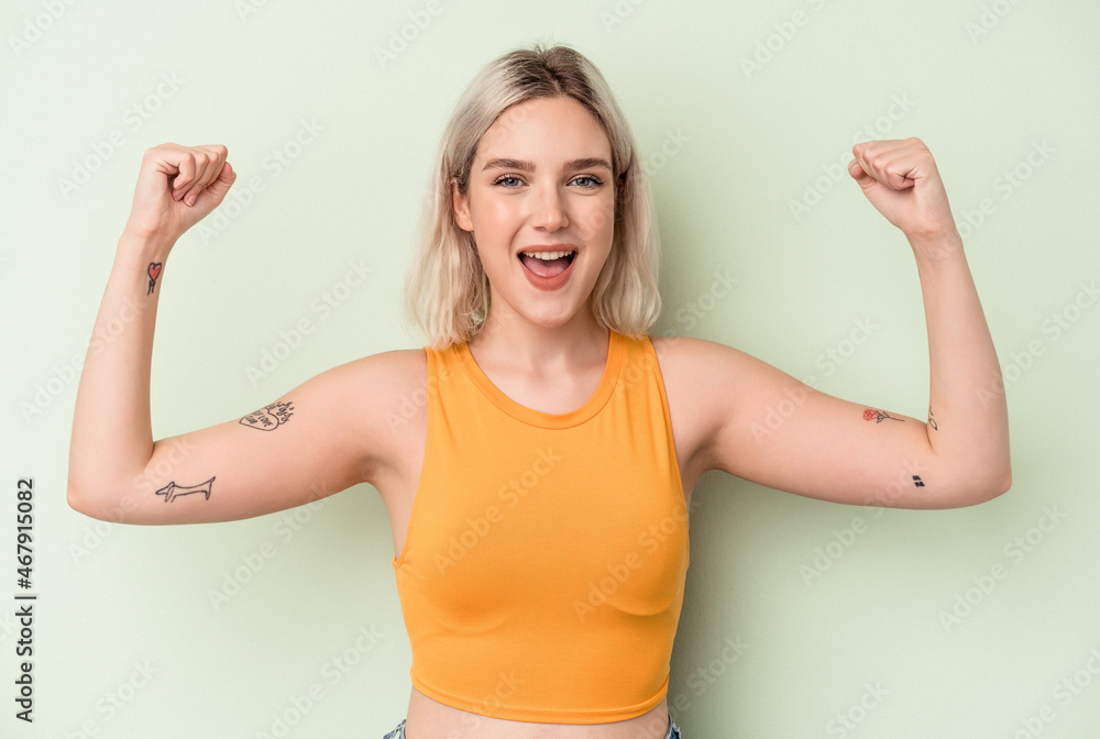 Fototapeta premium Young caucasian woman isolated on green background showing strength gesture with arms, symbol of feminine power