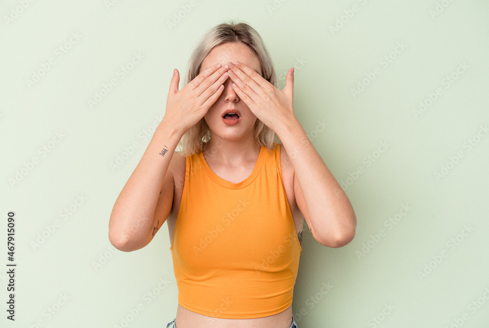 Young caucasian woman isolated on green background afraid covering eyes with hands.
