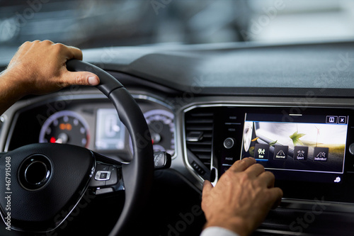 Close up of man touching multimedia screen of luxury car while sitting inside. Male customer testing modern innovative dashboard before buying vehicle. Selling and purchase concept.