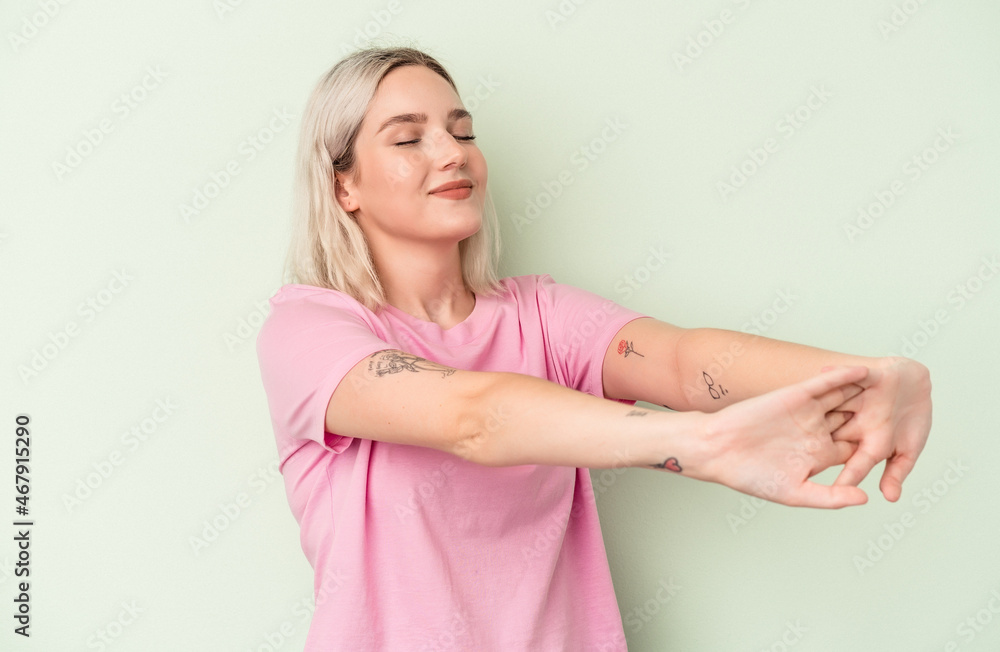 Young caucasian woman isolated on green background stretching arms, relaxed position. Young caucasian woman isolated on green background stretching arms, relaxed position.