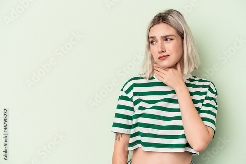 Young caucasian woman isolated on green background touching back of head, thinking and making a choice.