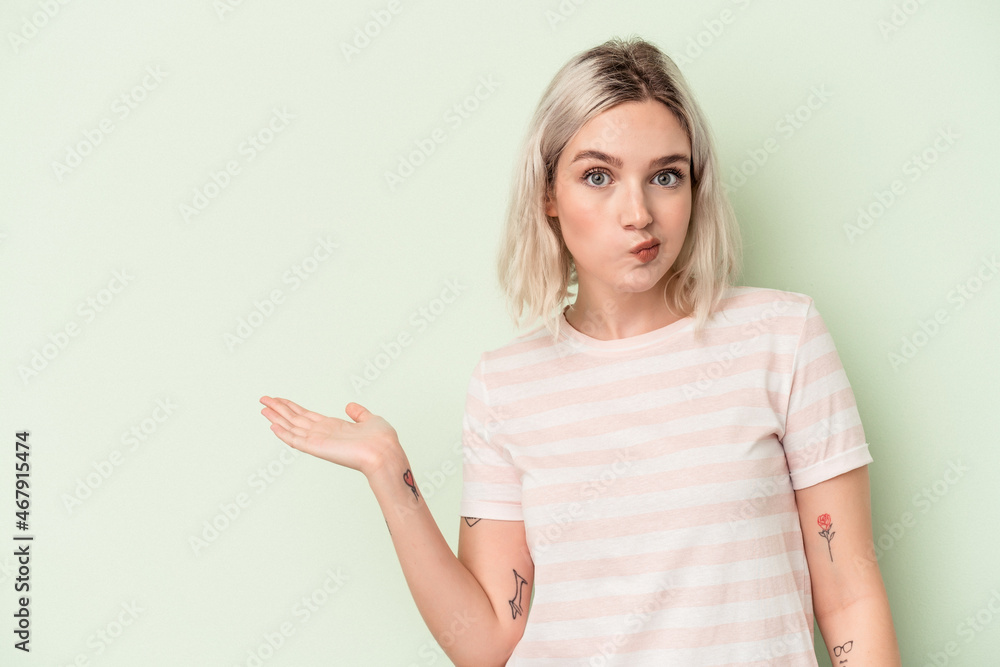 Young caucasian woman isolated on green background showing a copy space on a palm and holding another hand on waist. Young caucasian woman isolated on green background showing a copy space on a palm and holding another hand on waist.