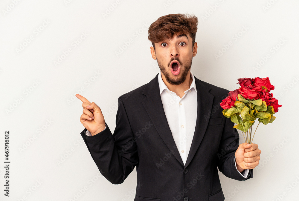 Young mixed race man holding bouquet of roses isolated on white background pointing to the side Young mixed race man holding bouquet of roses isolated on white background pointing to the side