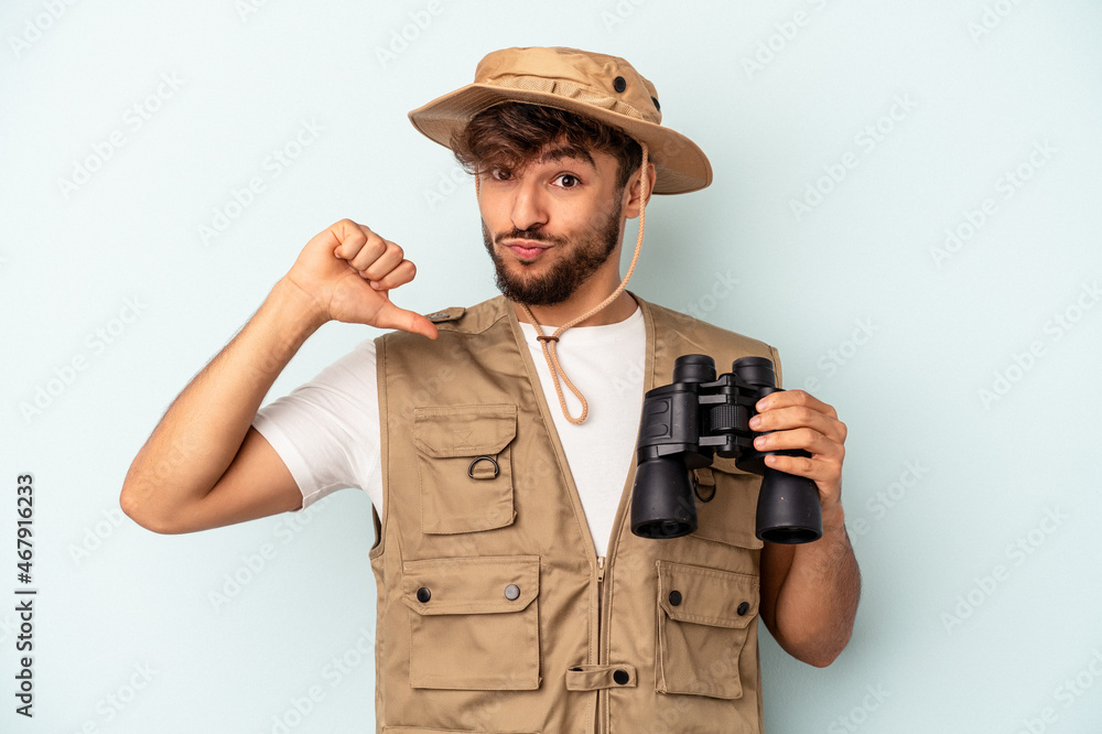 Young mixed race man holding binoculars isolated on blue background feels proud and self confident, example to follow. Young mixed race man holding binoculars isolated on blue background feels proud and self confident, example to follow.