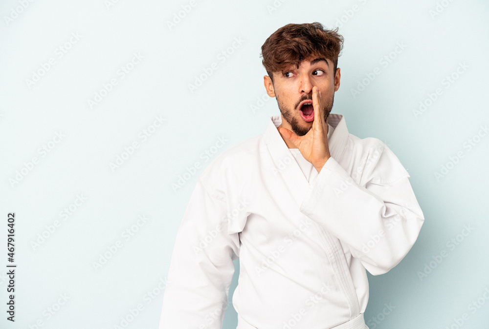 Young mixed race man doing karate isolated on blue background is saying a secret hot braking news and looking aside Young mixed race man doing karate isolated on blue background is saying a secret hot braking news and looking aside