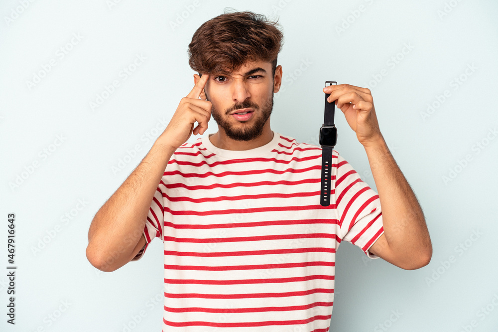 Young mixed race man holding a wrist watch isolated on blue background showing a disappointment gesture with forefinger. Young mixed race man holding a wrist watch isolated on blue background showing a disappointment gesture with forefinger.