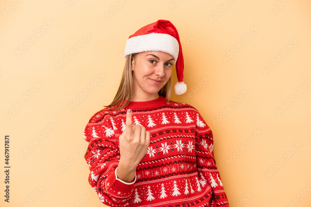 Young caucasian woman celebrating Christmas isolated on yellow background pointing with finger at you as if inviting come closer. Young caucasian woman celebrating Christmas isolated on yellow background pointing with finger at you as if inviting come closer.