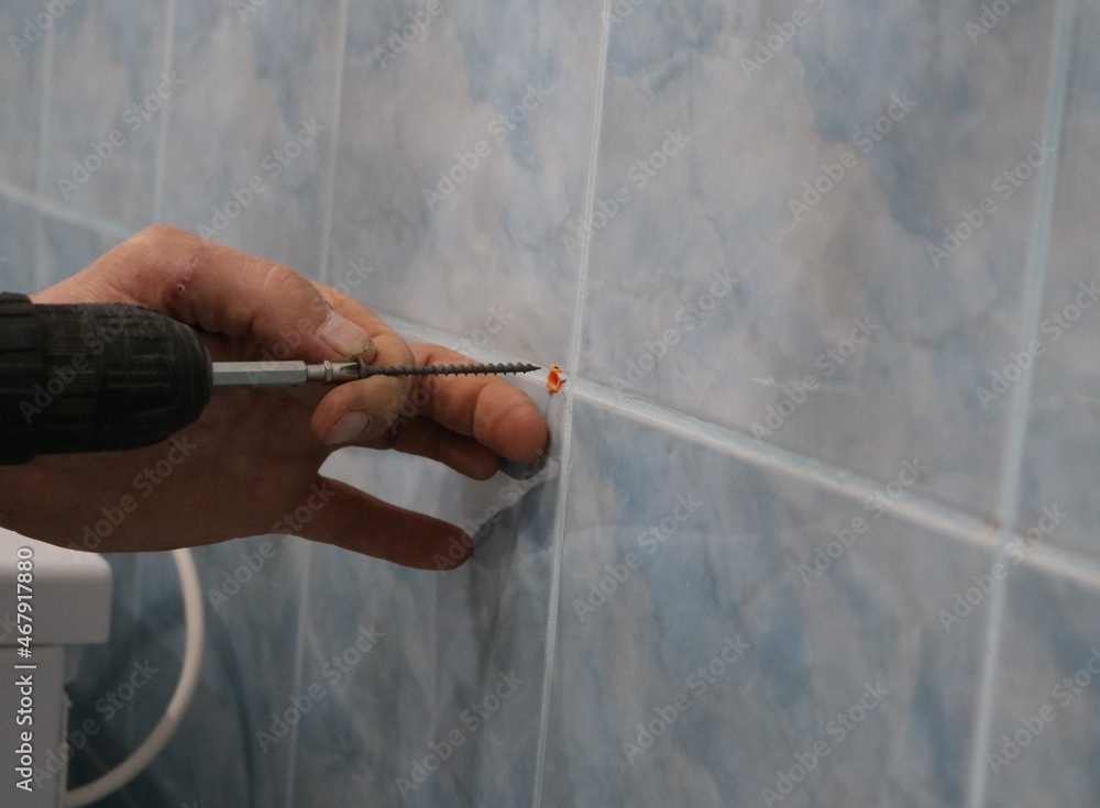 inserting a self-tapping screw at the tip of a screwdriver drill into a dowel driven into the wall for installing fasteners in the interior of the bathroom