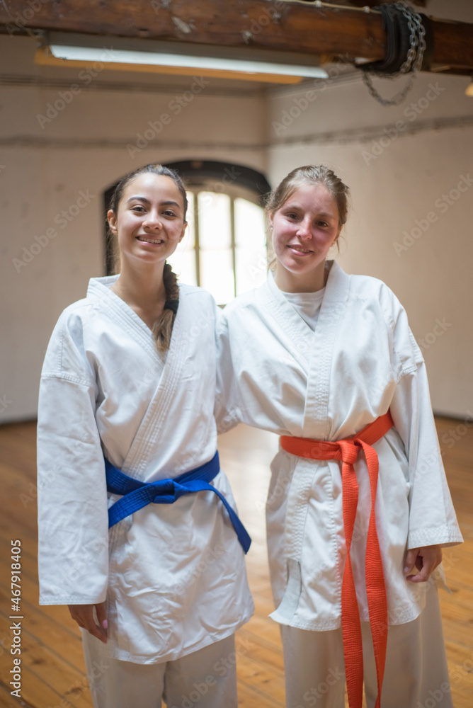 Fototapeta premium Happy female karate girls hugging in studio after class. Joyful Caucasian karate women resting after lesson in sports academy. Sports, martial arts, healthy lifestyle concept