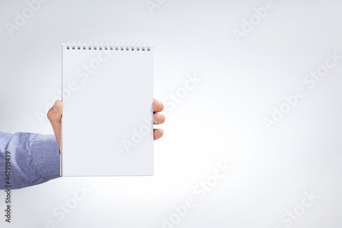 Male hand holding notebook on light grey background. Mock-up.