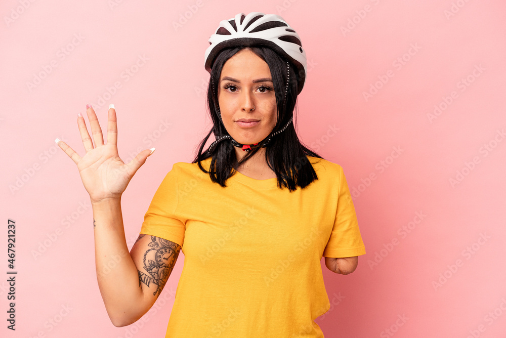 Young caucasian woman with one arm wearing a bike helmet isolated on pink background smiling cheerful showing number five with fingers. Young caucasian woman with one arm wearing a bike helmet isolated on pink background smiling cheerful showing number five with fingers.