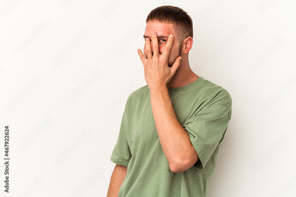 Young caucasian man with diastema isolated on white background blink at the camera through fingers, embarrassed covering face. Young caucasian man with diastema isolated on white background blink at the camera through fingers, embarrassed covering face.