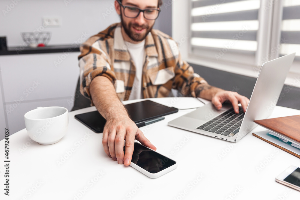Satisfied man picks up a mobile phone from the table during a break between work Satisfied man picks up a mobile phone from the table during a break between work