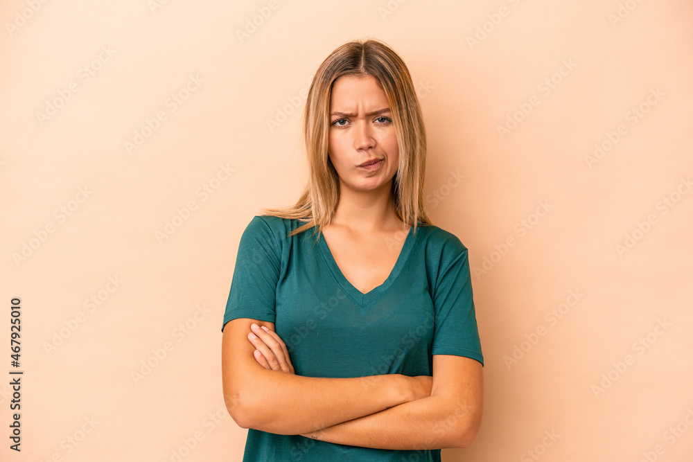 Young caucasian woman isolated on beige background frowning face in displeasure, keeps arms folded. Young caucasian woman isolated on beige background frowning face in displeasure, keeps arms folded.