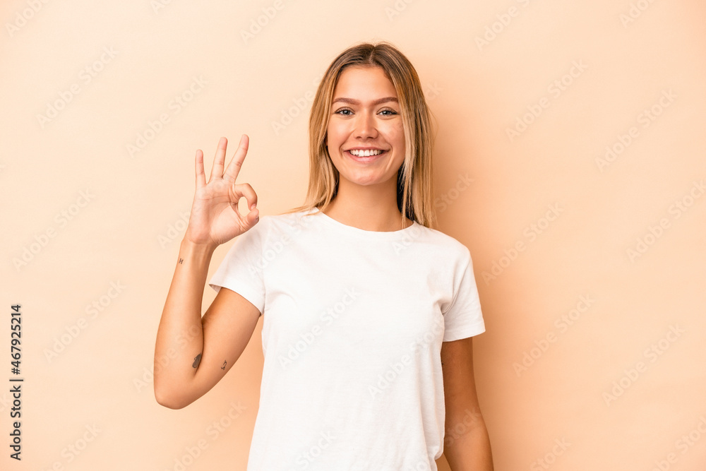 Young caucasian woman isolated on beige background cheerful and confident showing ok gesture. Young caucasian woman isolated on beige background cheerful and confident showing ok gesture.