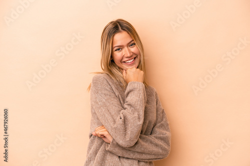 Young caucasian woman isolated on beige background smiling happy and confident, touching chin with hand.