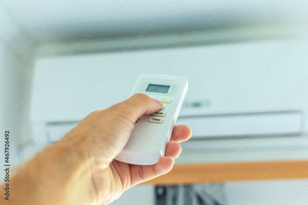 The hand turns on the air conditioner using the remote control. There is an air conditioner on the wall in the background. The hand turns on the air conditioner using the remote control. There is an air conditioner on the wall in the background.
