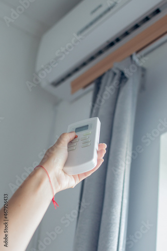 Male hand holds a remote control of air conditioner. There is an air conditioner on the wall in the background. Home climate control concept.