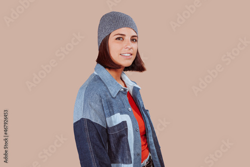 Cheerful beautiful caucasian woman looking at camera wearing urban outfit posing in studio. Photo of a young girl isolated on a beige background. photo