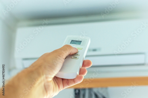 The hand turns on the air conditioner using the remote control. There is an air conditioner on the wall in the background.