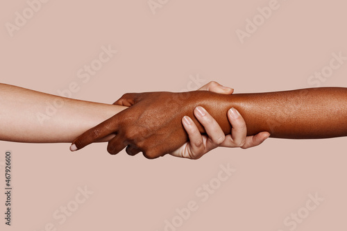 Close up multiracial woman couple with black and caucasian hands holding each other wrist in tolerance unity love and anti racism concept.