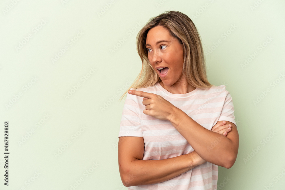 Young caucasian woman isolated on green background points with thumb finger away, laughing and carefree. Young caucasian woman isolated on green background points with thumb finger away, laughing and carefree.