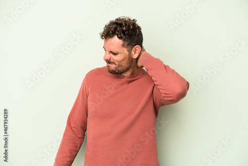 Young caucasian man isolated on green background having a neck pain due to stress, massaging and touching it with hand.