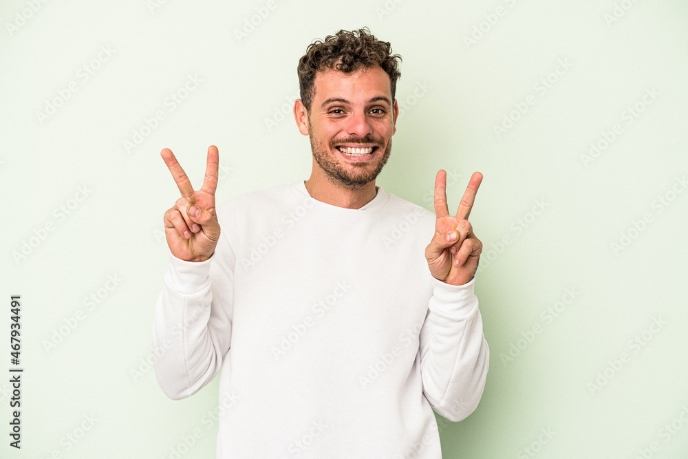 Young caucasian man isolated on green background showing victory sign and smiling broadly. Young caucasian man isolated on green background showing victory sign and smiling broadly.