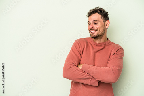 Young caucasian man isolated on green background smiling confident with crossed arms.