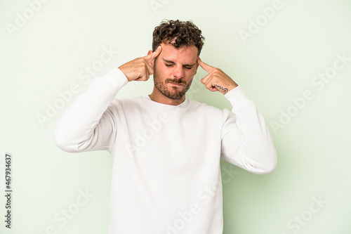 Young caucasian man isolated on green background focused on a task, keeping forefingers pointing head.