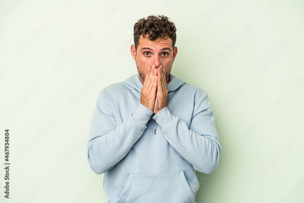 Young caucasian man isolated on green background covering mouth with hands looking worried. Young caucasian man isolated on green background covering mouth with hands looking worried.