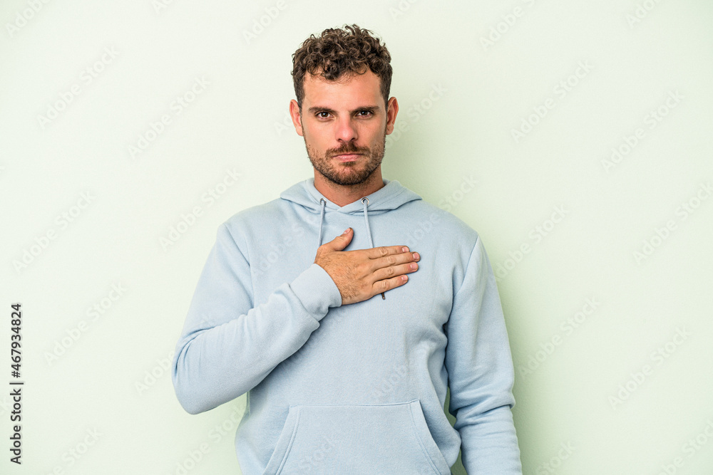 Young caucasian man isolated on green background taking an oath, putting hand on chest. Young caucasian man isolated on green background taking an oath, putting hand on chest.