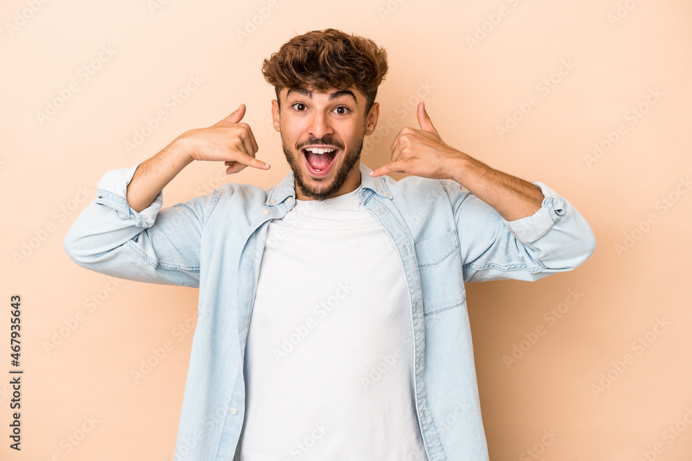 Young arab man isolated on beige background showing a mobile phone call gesture with fingers. Young arab man isolated on beige background showing a mobile phone call gesture with fingers.