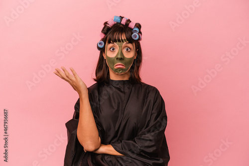 Young mixed race woman waiting in a Beaty salon isolated on pink background shrugs shoulders and open eyes confused. © Asier
