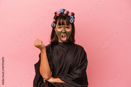 Young mixed race woman waiting in a Beaty salon isolated on pink background screaming very angry and aggressive. © Asier