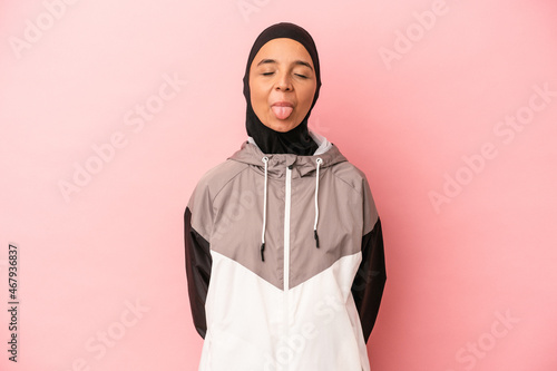 Young Arab woman with sport burqa isolated on pink background funny and friendly sticking out tongue.